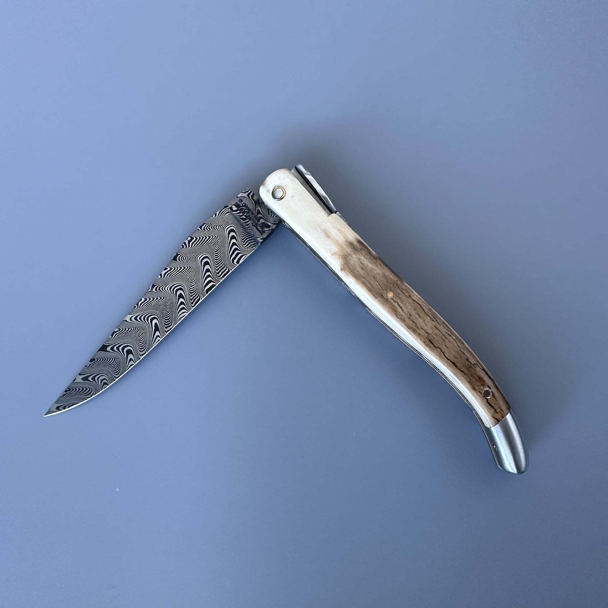 A folding pocket knife with a Damascus steel blade and a natural ivory crust handle, reverse side.