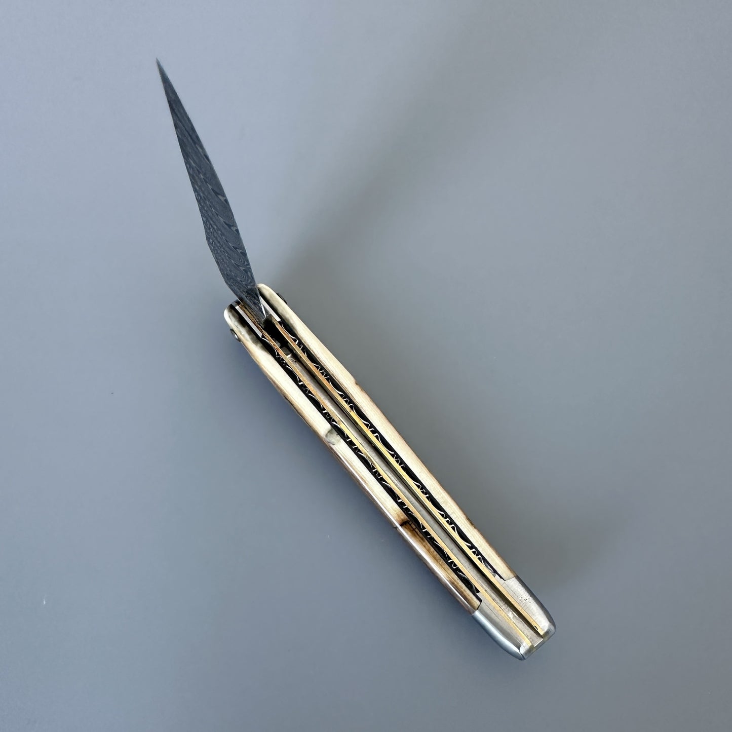 A folding pocket knife inner spine and a polished brass metal handle, shown open on a neutral gray background.