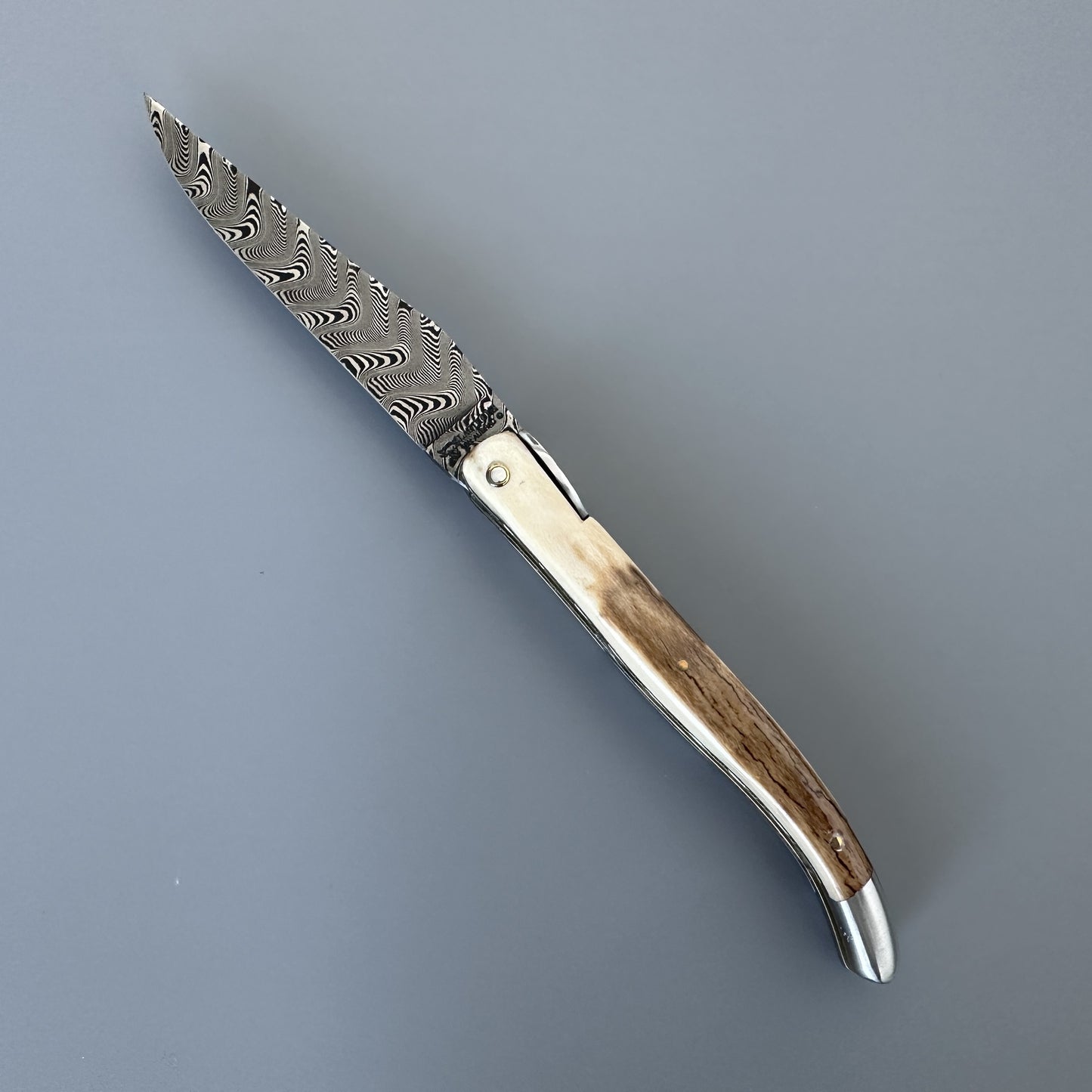 A folding pocket knife with a Damascus steel blade, a natural crust handle shown fully opened