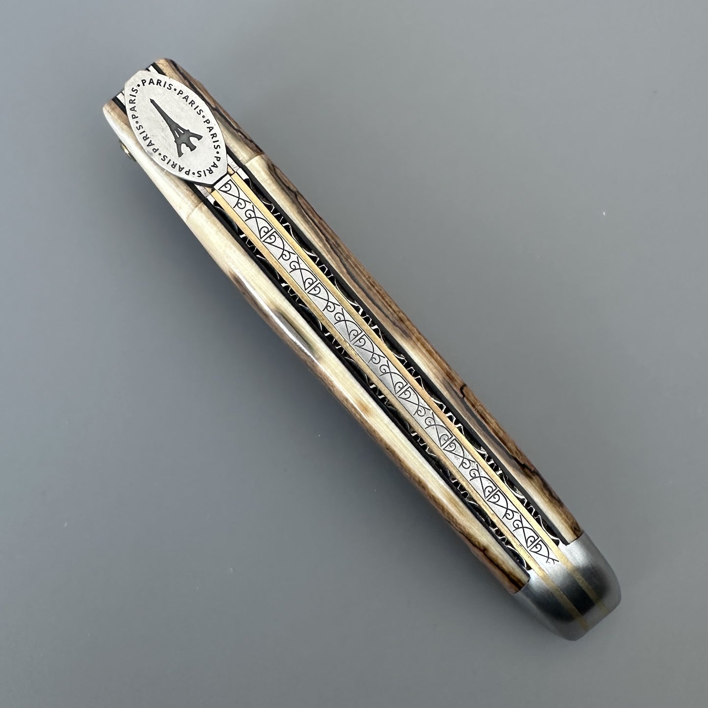 A folding pocket knife featuring black engraved geometric patterns and a silver-toned metal end cap, shown on a neutral gray background.