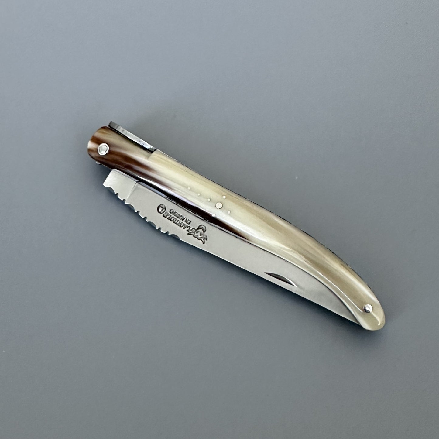 A closed folding pocket knife with a polished silver metal blade and solid horn handle, featuring a dark brown wood inlay near the pivot, shown on a neutral gray background.