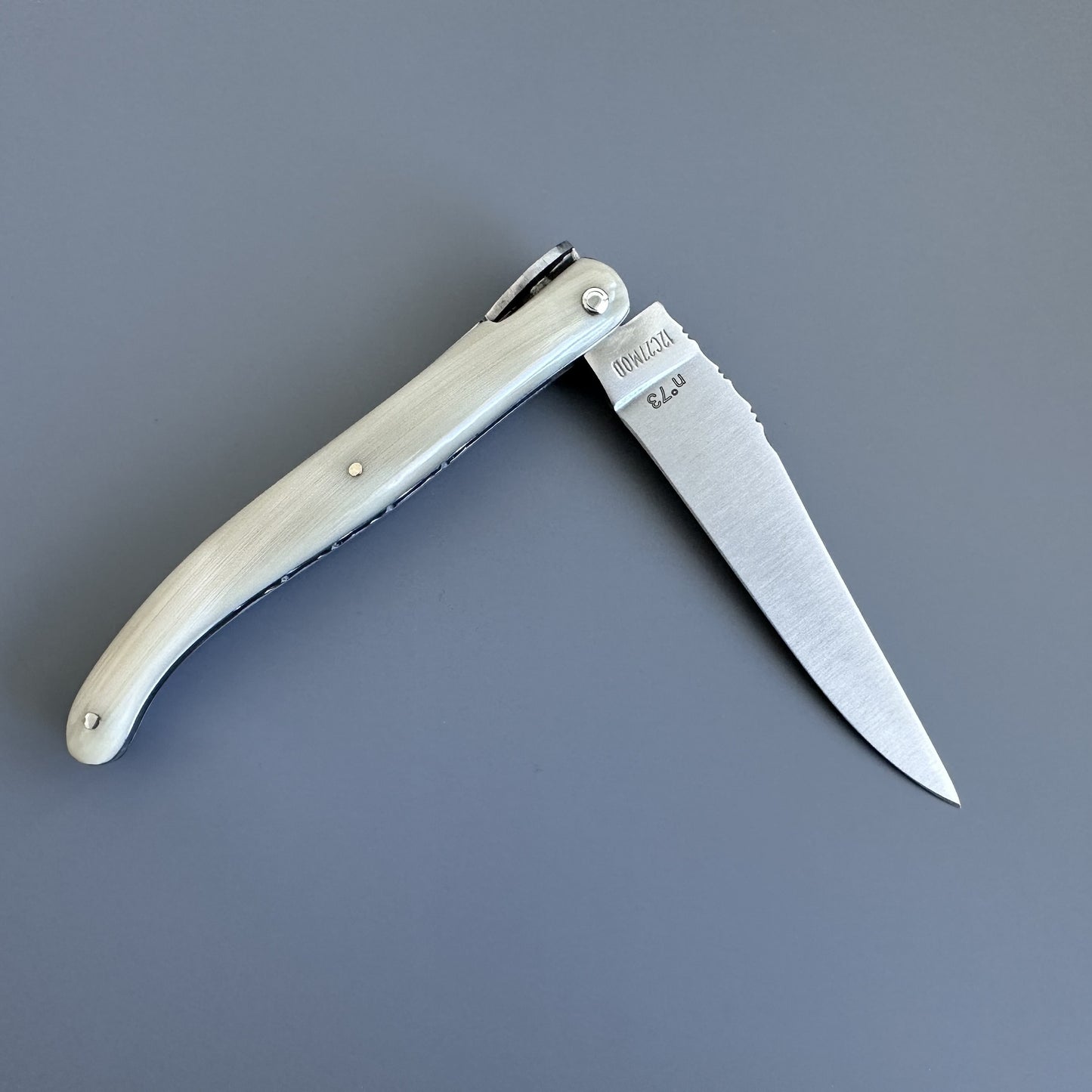 A folding pocket knife with a cream-colored bone handle and a silver steel blade, shown open on a solid gray background. 