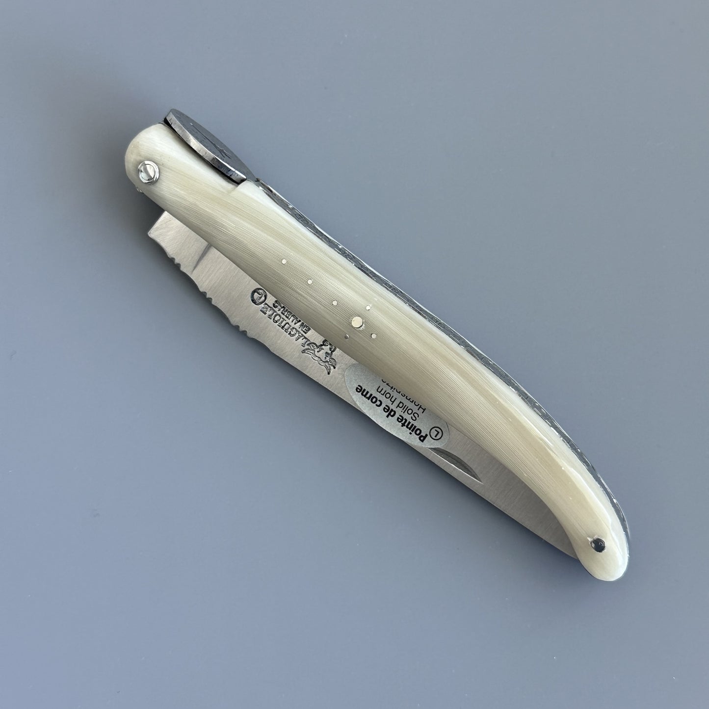 A folding pocket knife with a cream-colored handle and a silver stainless steel blade, shown open on a solid gray background. The brand Laguiole en Aubrac is engraved on the blade.