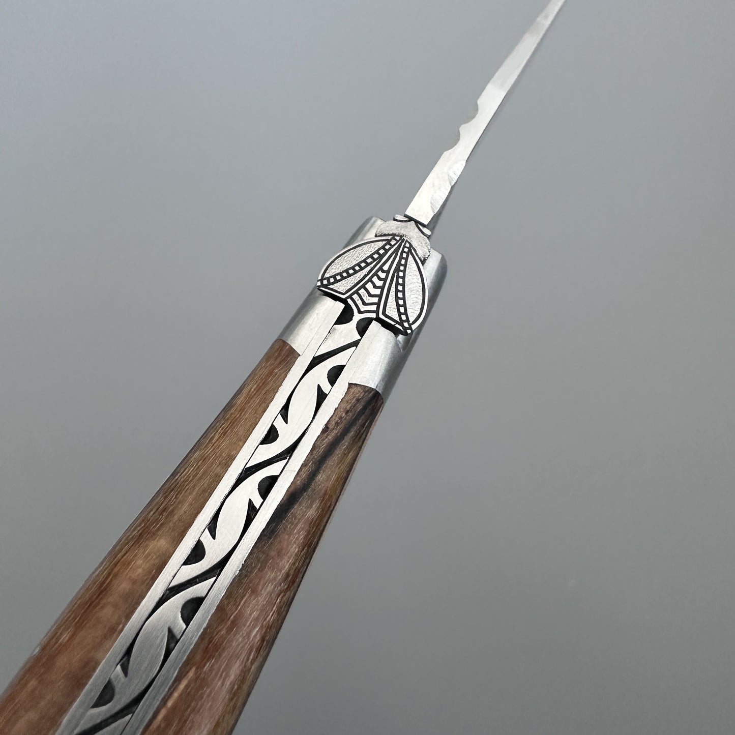Close-up of the Belle knife's hand-carved bee bolster and Aubrac wood grain, angled toward the blade tip
