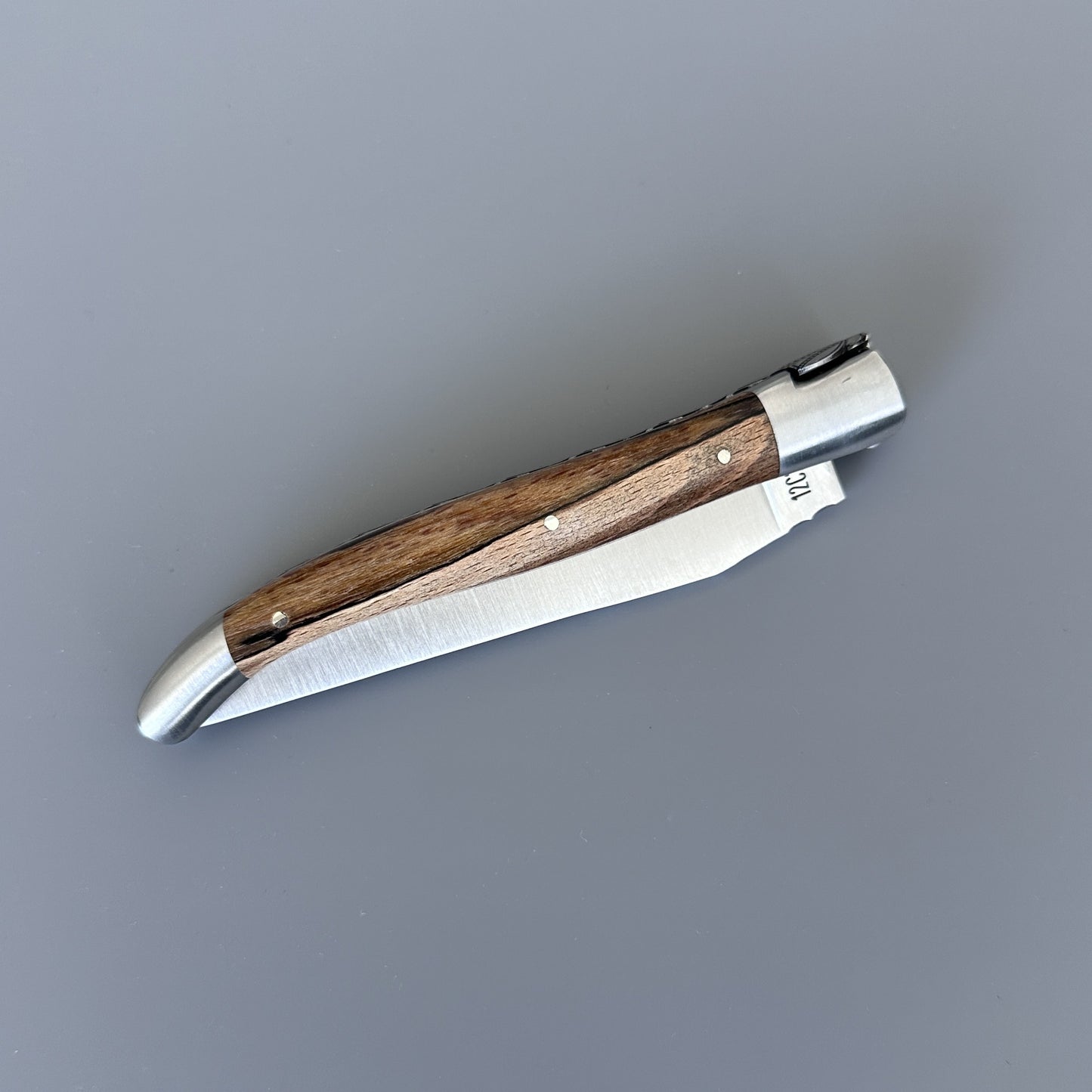 Closed Laguiole en Aubrac Belle knife with Aubrac wood handle, shown diagonally with blade edge and pin detail visible