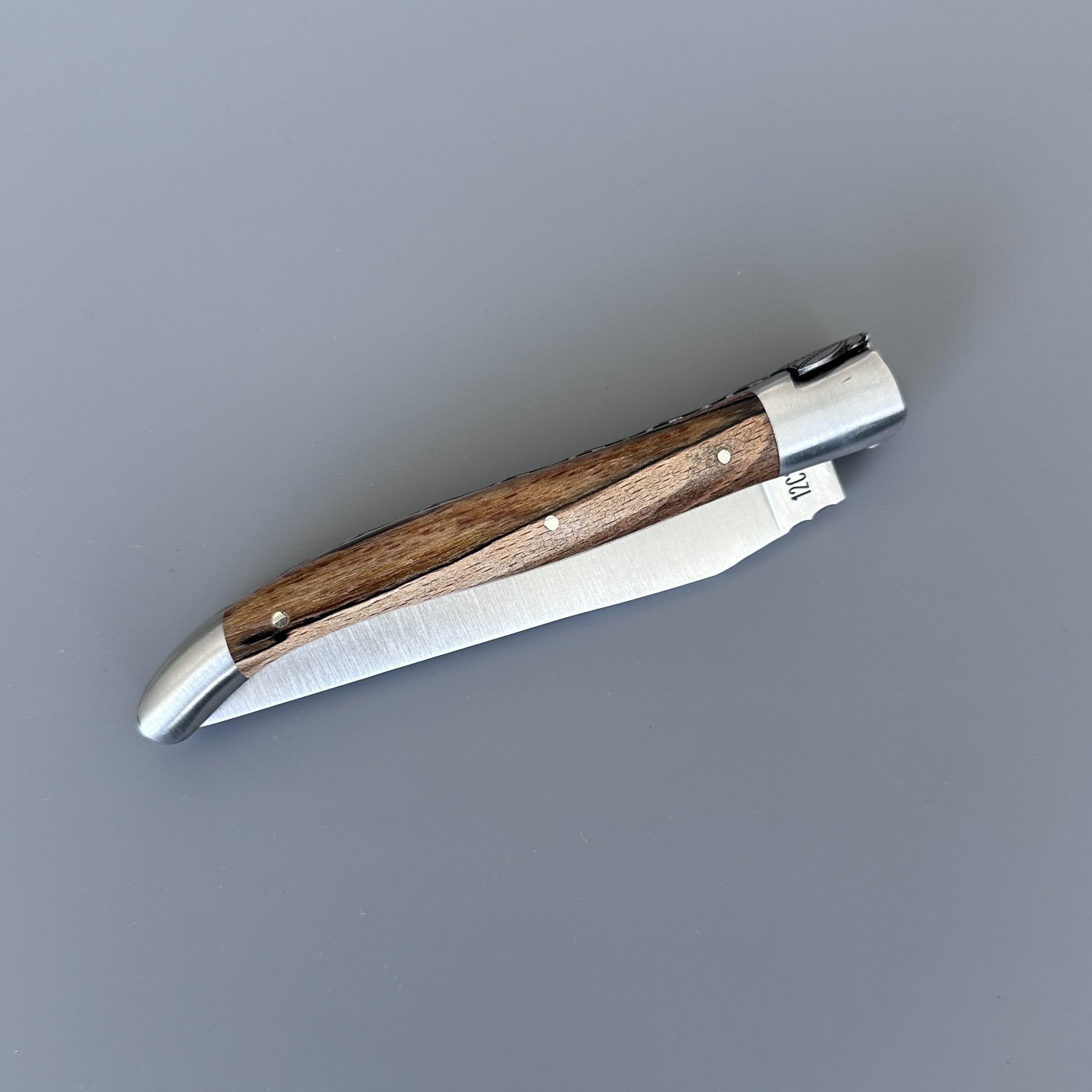 Closed Laguiole en Aubrac Belle knife with Aubrac wood handle, shown diagonally with blade edge and pin detail visible