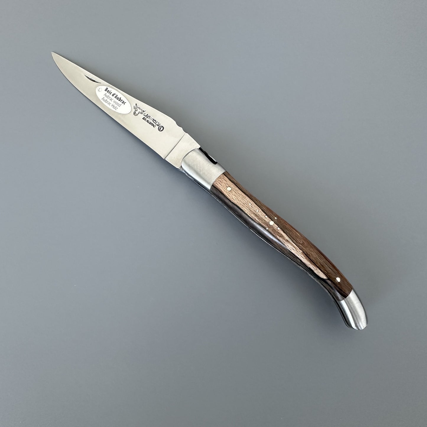 Open Belle folding knife with etched blade and Aubrac wood handle, shown blade-right with maker's mark