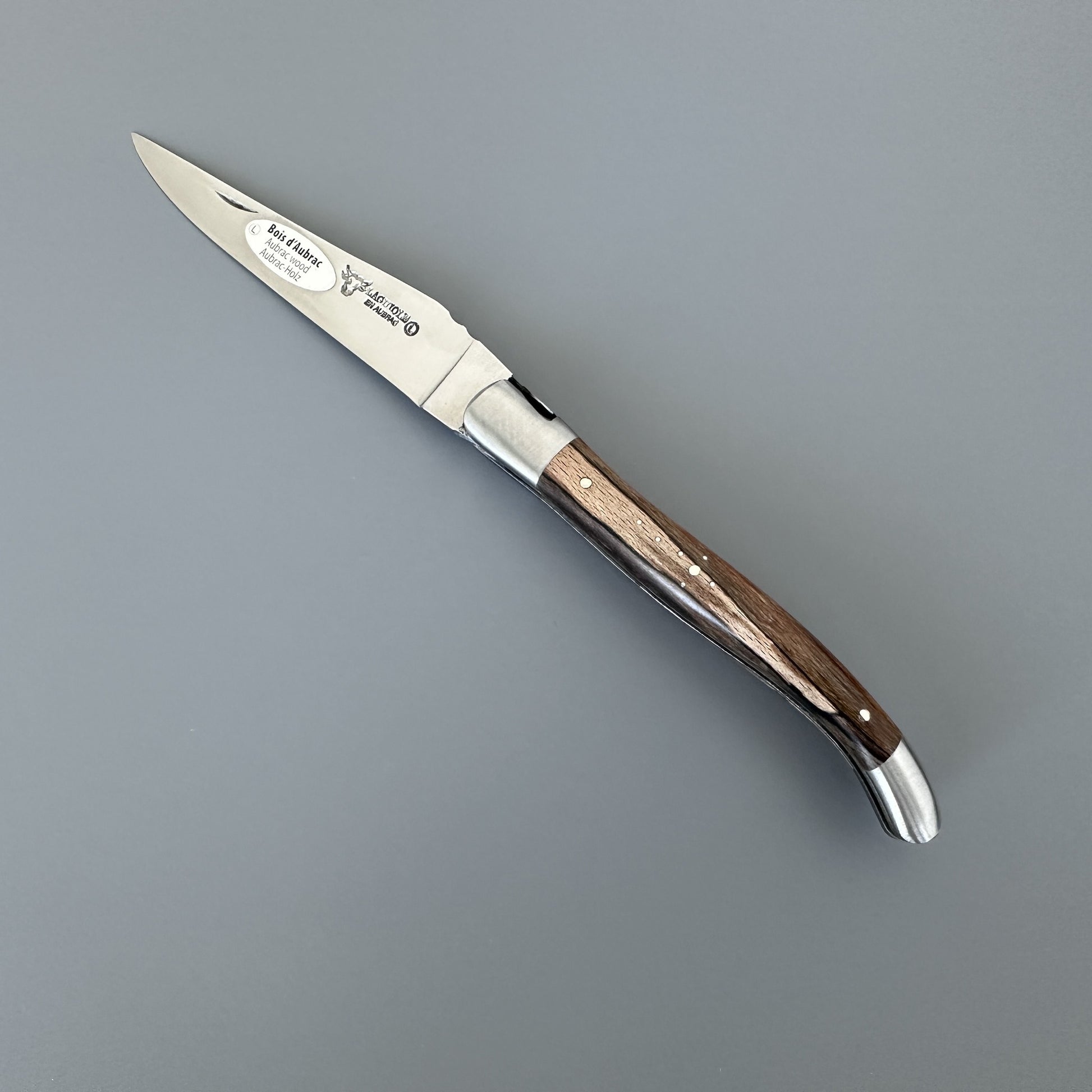 Open Belle folding knife with etched blade and Aubrac wood handle, shown blade-right with maker's mark