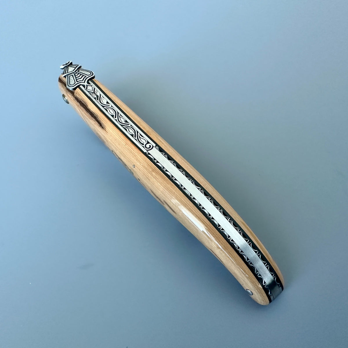 Closed Laguiole en Aubrac Belle Piece L0512IVH/FS-BP53 highlighting its decorated spine and light-caramel handle.