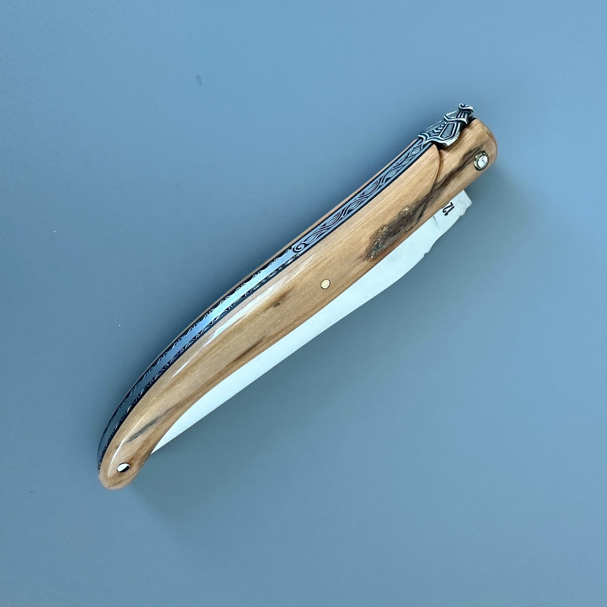 A folding pocket knife with a natural light caramel handle shown closed on a solid blue-gray background.