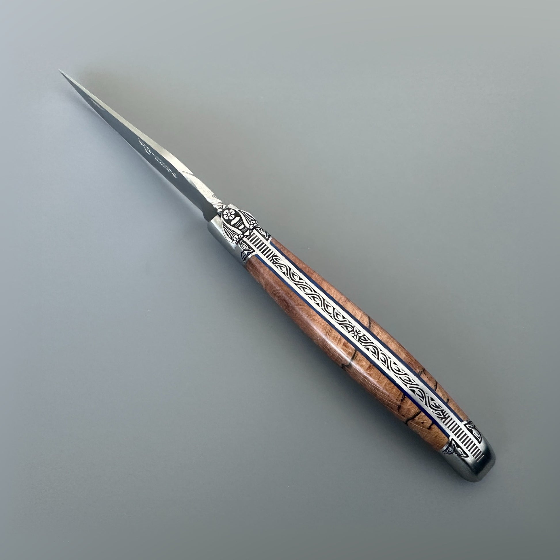 Open front view of a Laguiole en Aubrac Belle Piece folding knife with wood handle, blue spacer and engraved bolsters