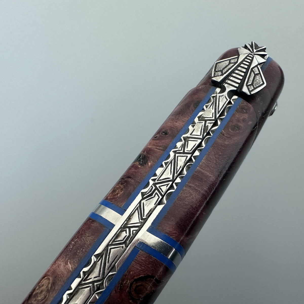 Laguiole en Aubrac close-up of a folding pocket knife handle with Wine poplar wood over light gray background.