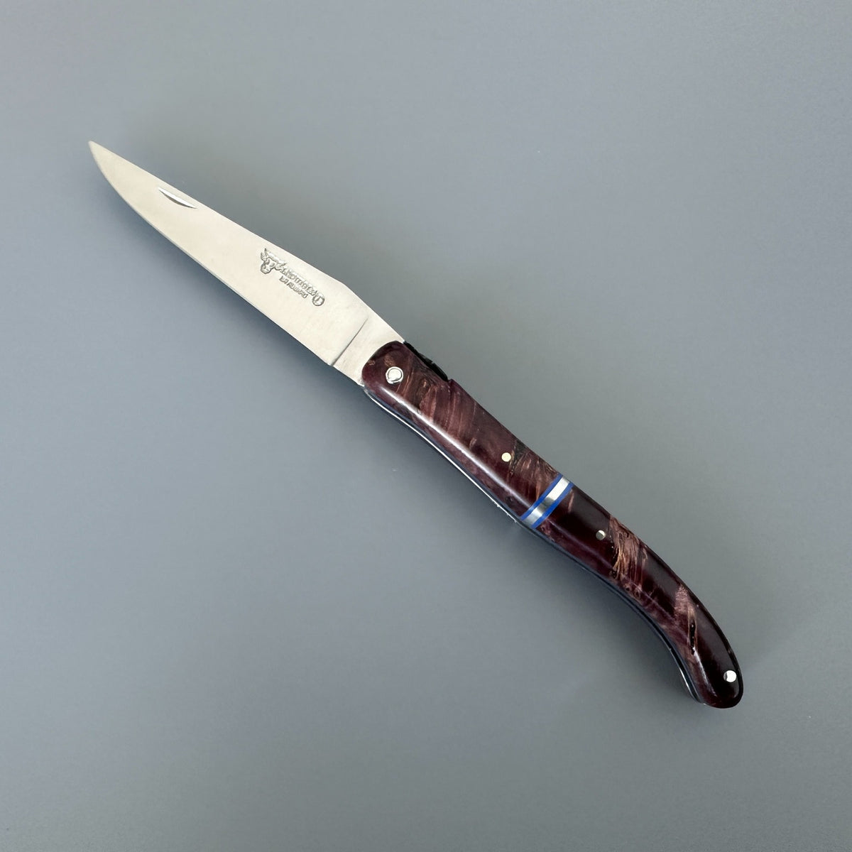 Laguiole en Aubrac folding pocket knife with a satin-finished silver blade and a dark reddish-brown wood-grain handle, shown on a neutral gray background.