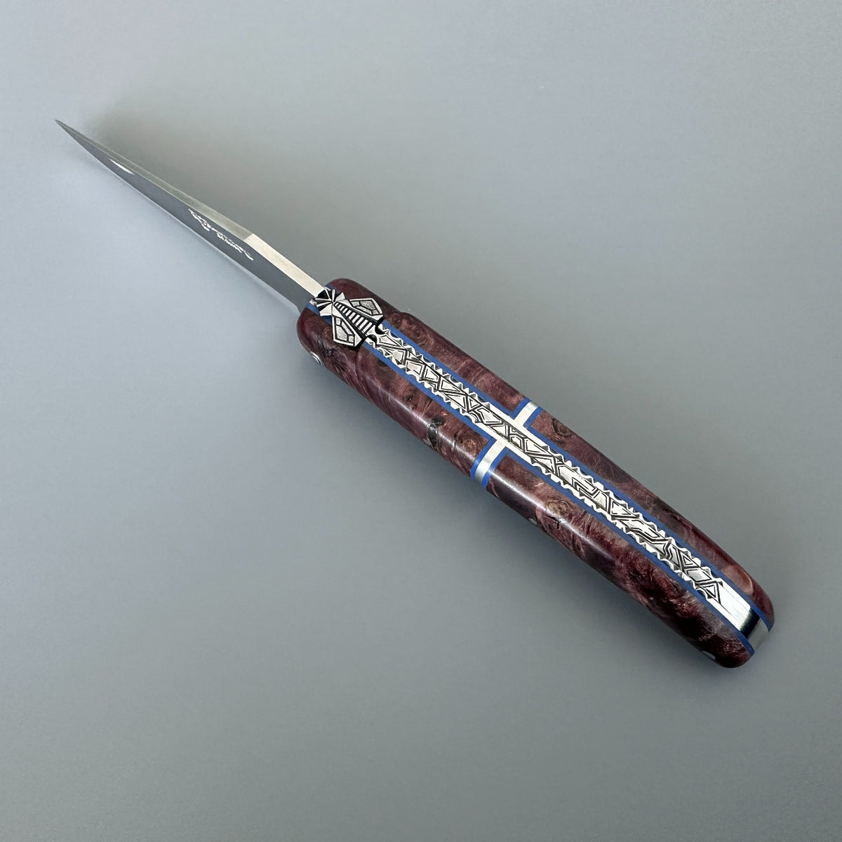 Laguiole en Aubrac folding pocket knife with a polished silver blade and a marbled reddish-brown handle featuring silver and blue inlay details, shown on a neutral gray background.