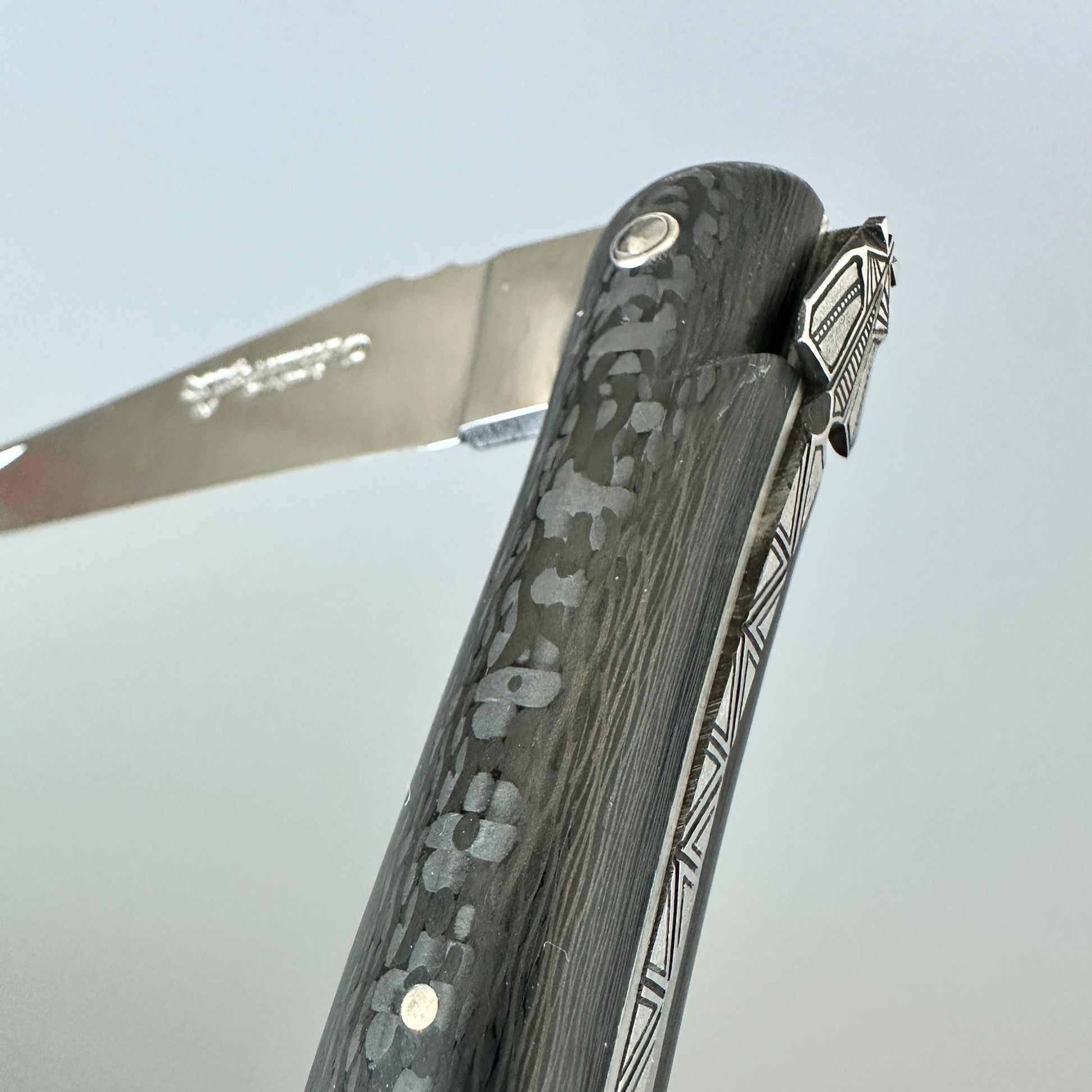 Close-up of the carbon handle and partly open blade on a Laguiole en Aubrac Belle Piece Carbon folding knife.