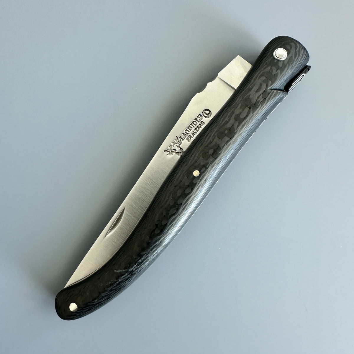 Closed Laguiole en Aubrac Belle Piece Carbon folding knife with the blade logo visible beside its curved carbon handle.