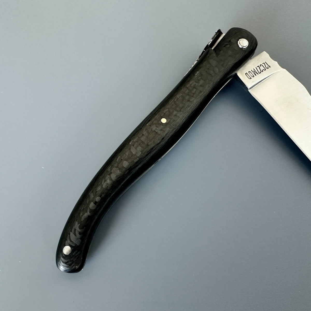 Detail of the patterned carbon handle, pivot pin and decorated metal spine on a Laguiole en Aubrac Belle Piece Carbon knife.