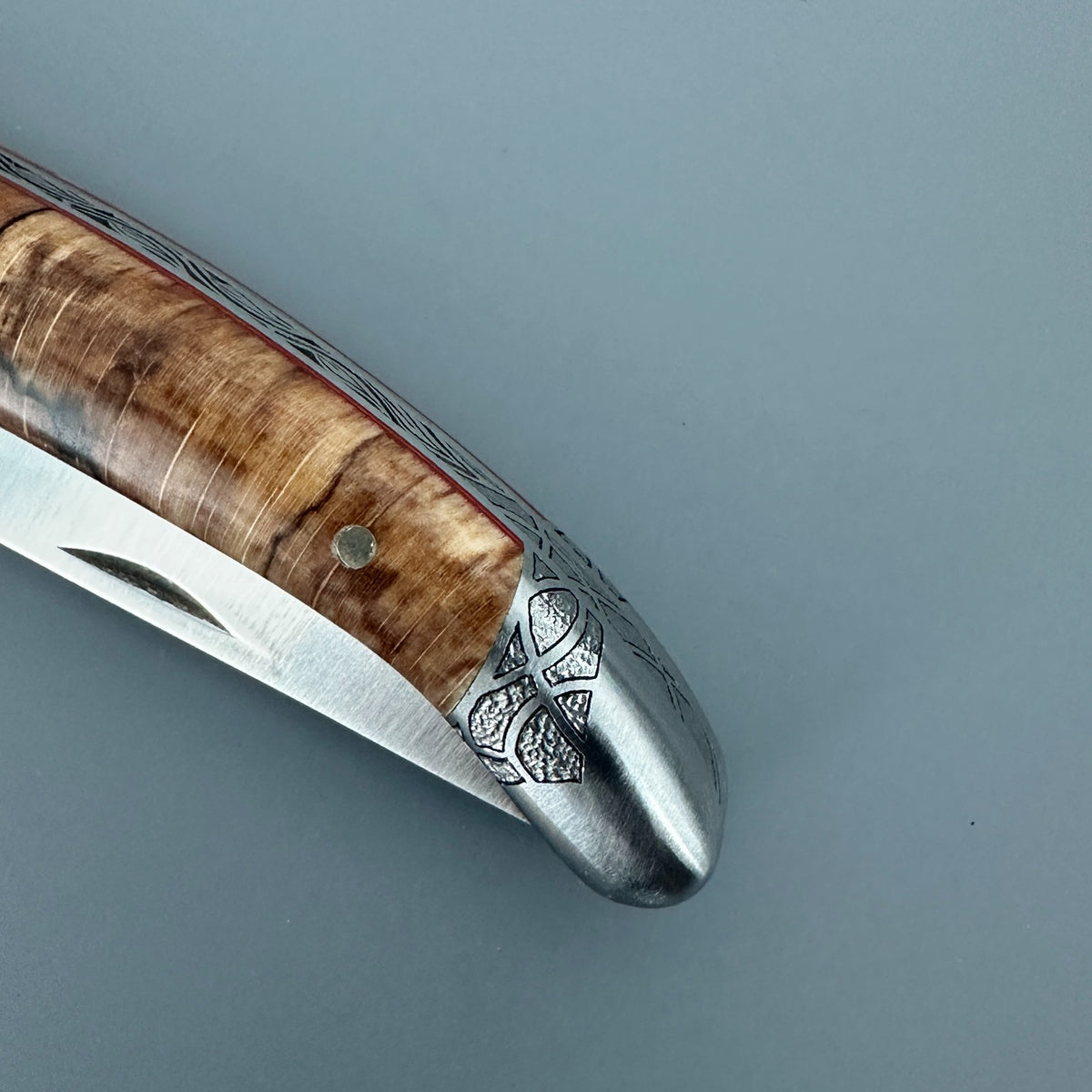 Close-up of the engraved rear bolster, wood handle and partially closed blade of a Laguiole en Aubrac Belle Piece