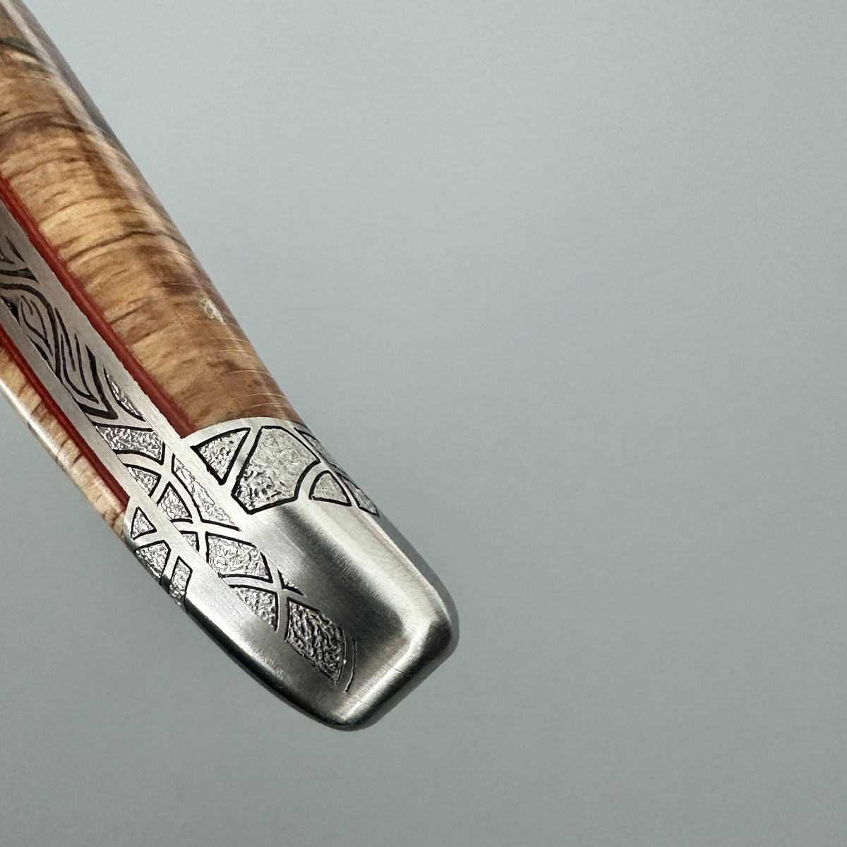 Detailed view of the engraved end bolster, hand-filed spine and red spacer on a Laguiole en Aubrac Belle Piece