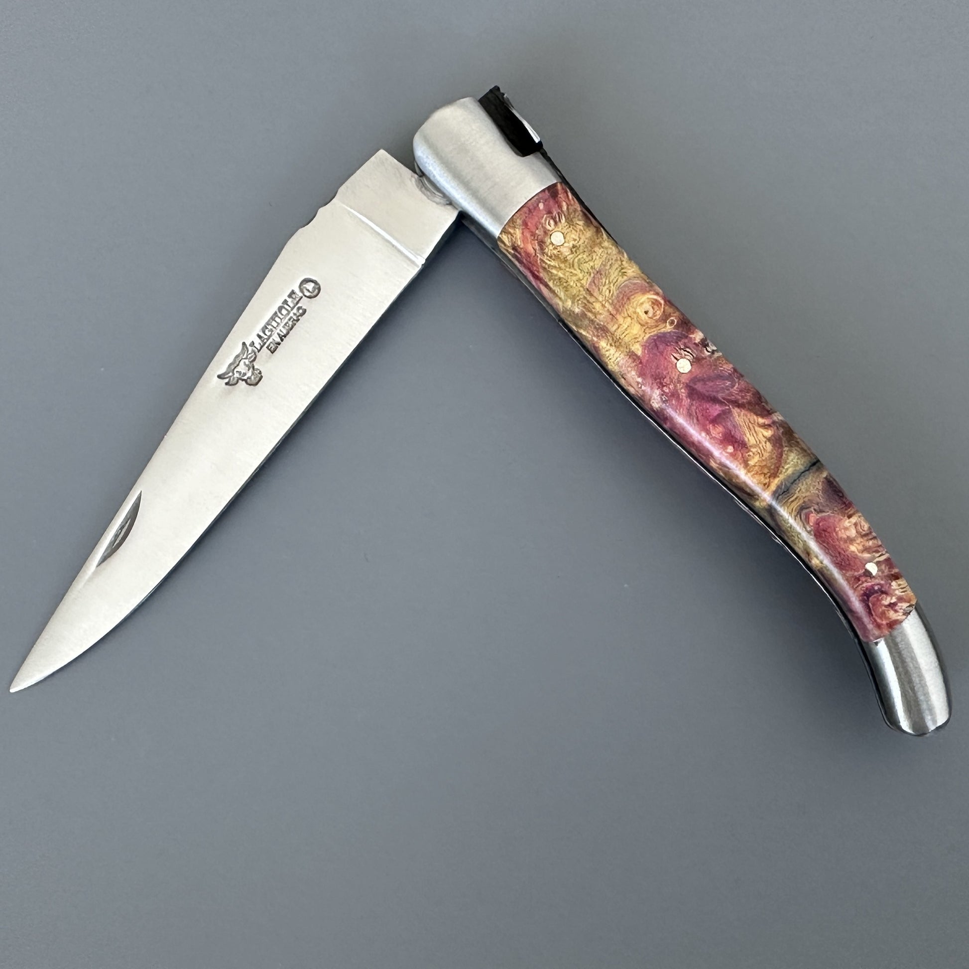 Closed Belle knife with yellow and burgundy elder burl handle and brand stamp on the blade