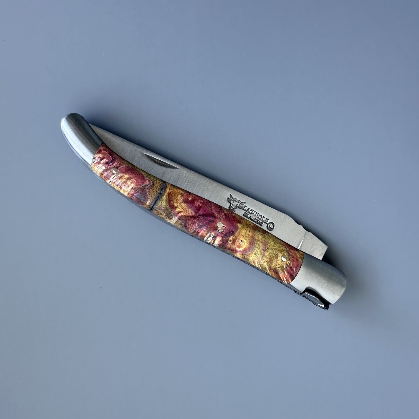 Closed Belle knife with gold and red elder burl handle, showing the maker's mark on the blade