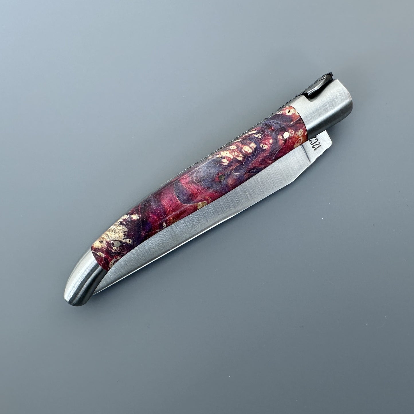 Closed Belle knife with gold and burgundy elder burl handle and brand stamp on the blade