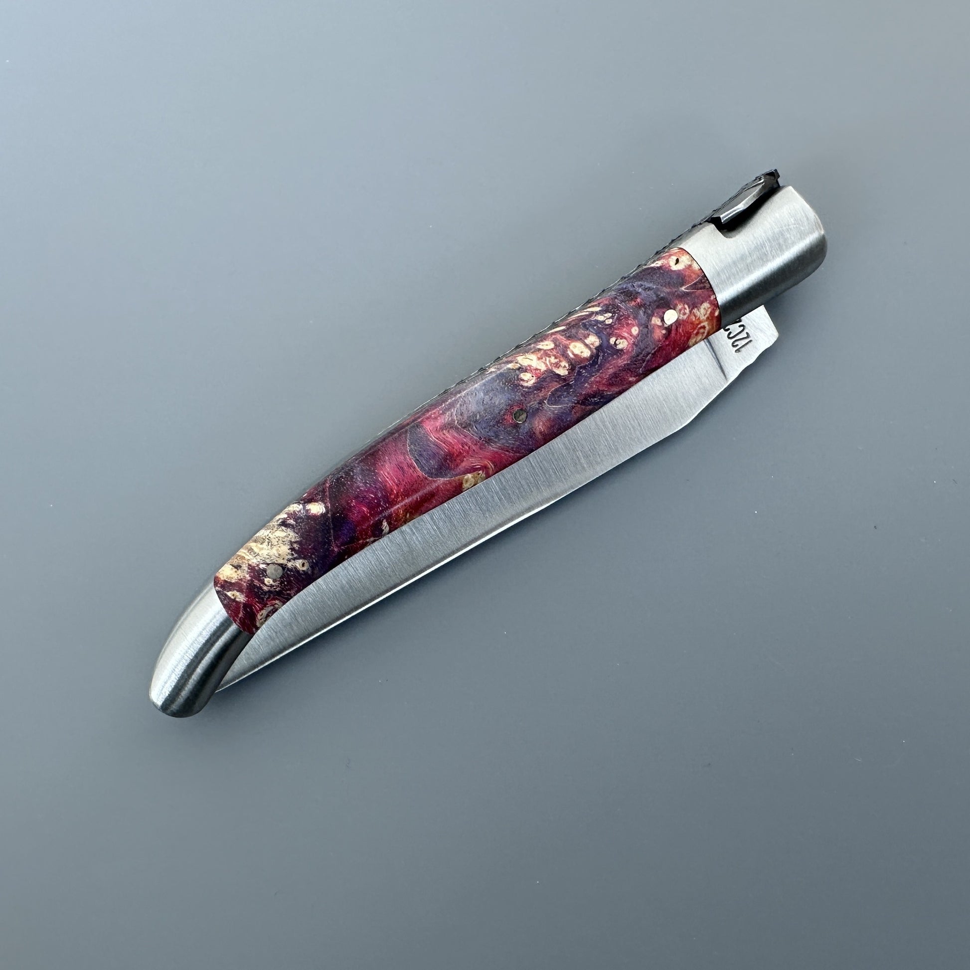 Closed Belle knife with gold and burgundy elder burl handle and brand stamp on the blade