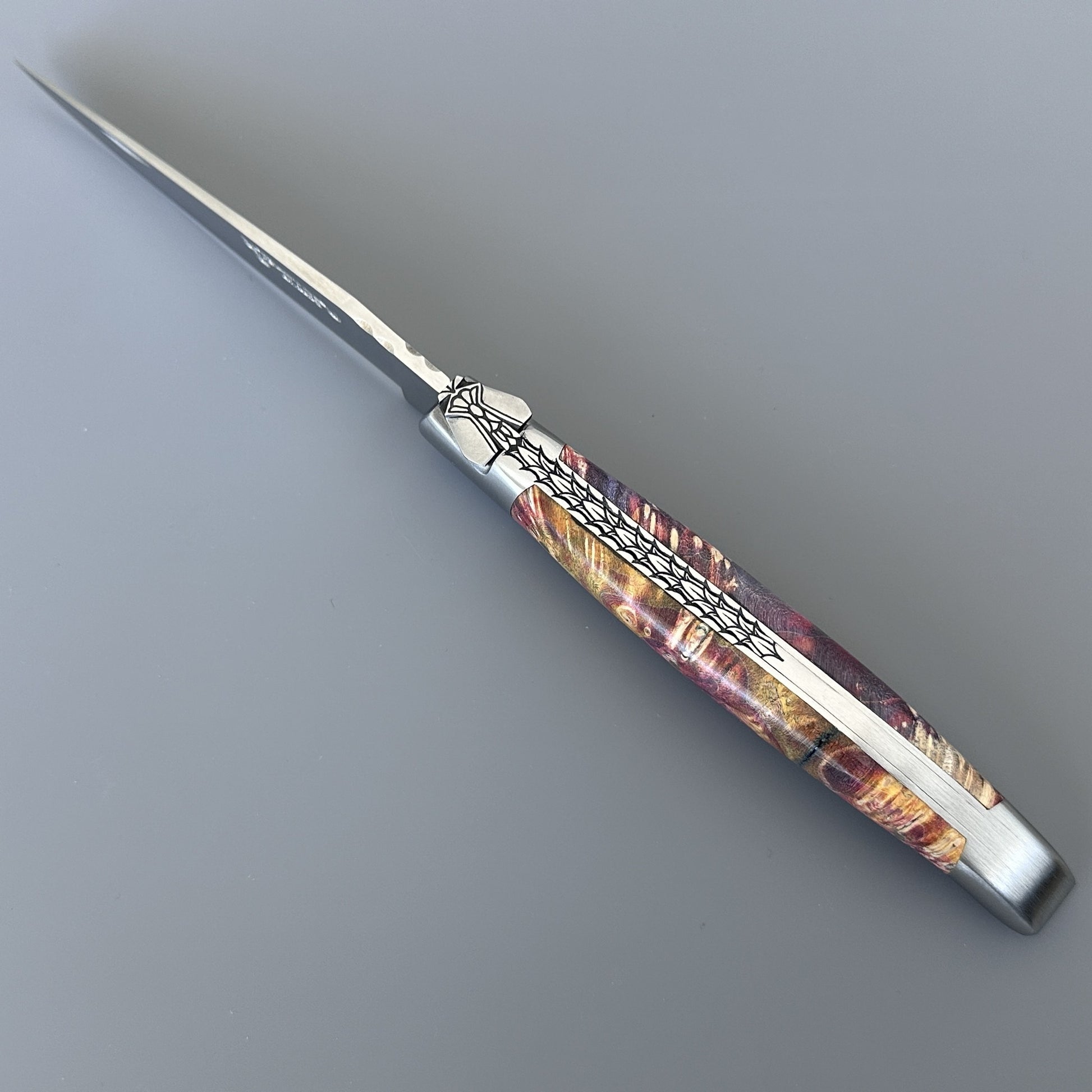 Diagonal close-up of an open Belle knife showing the carved bee bolster and vividly grained elder burl scales