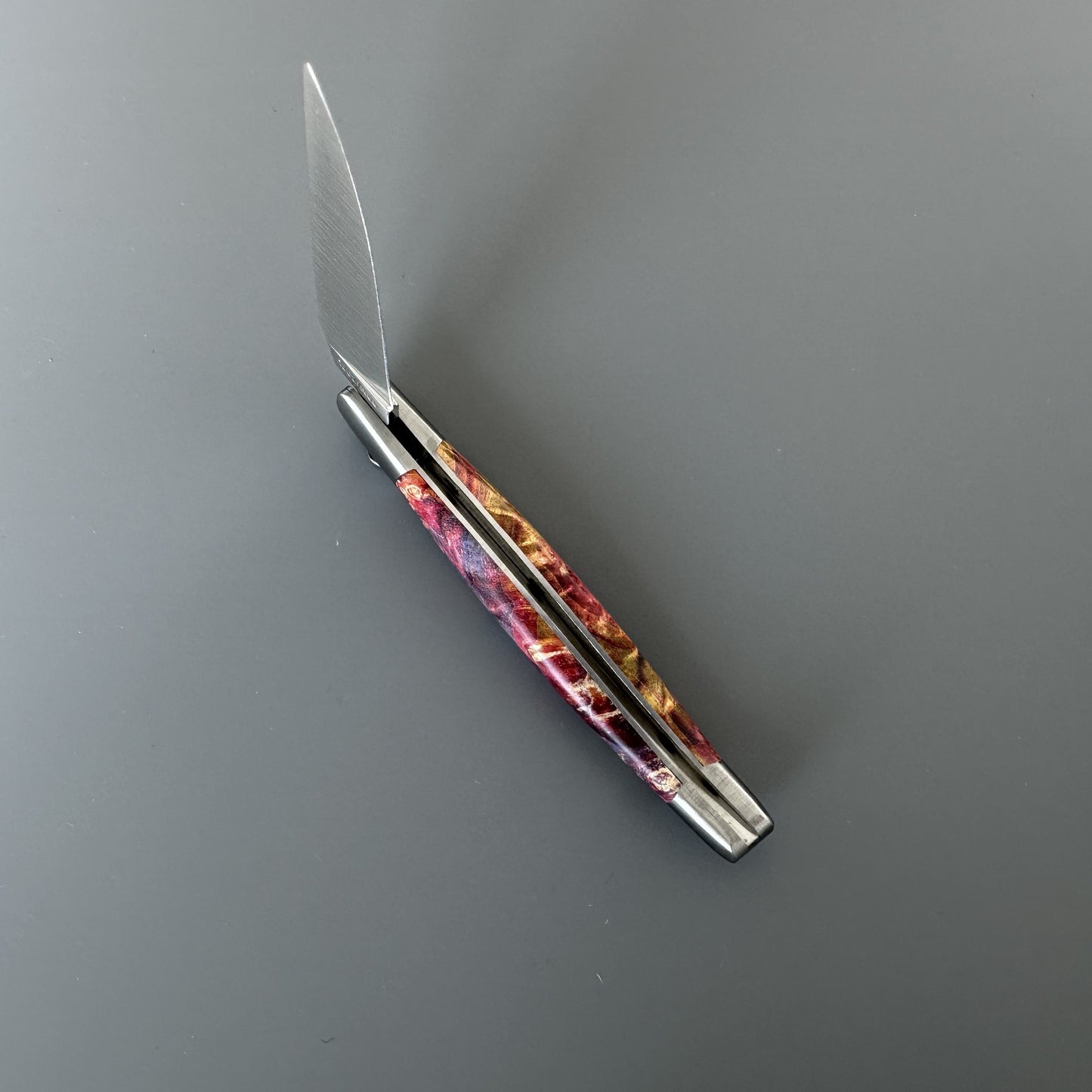 Open Belle folding knife with polished blade partly unfolded, red-gold elder burl handle, shown blade-left