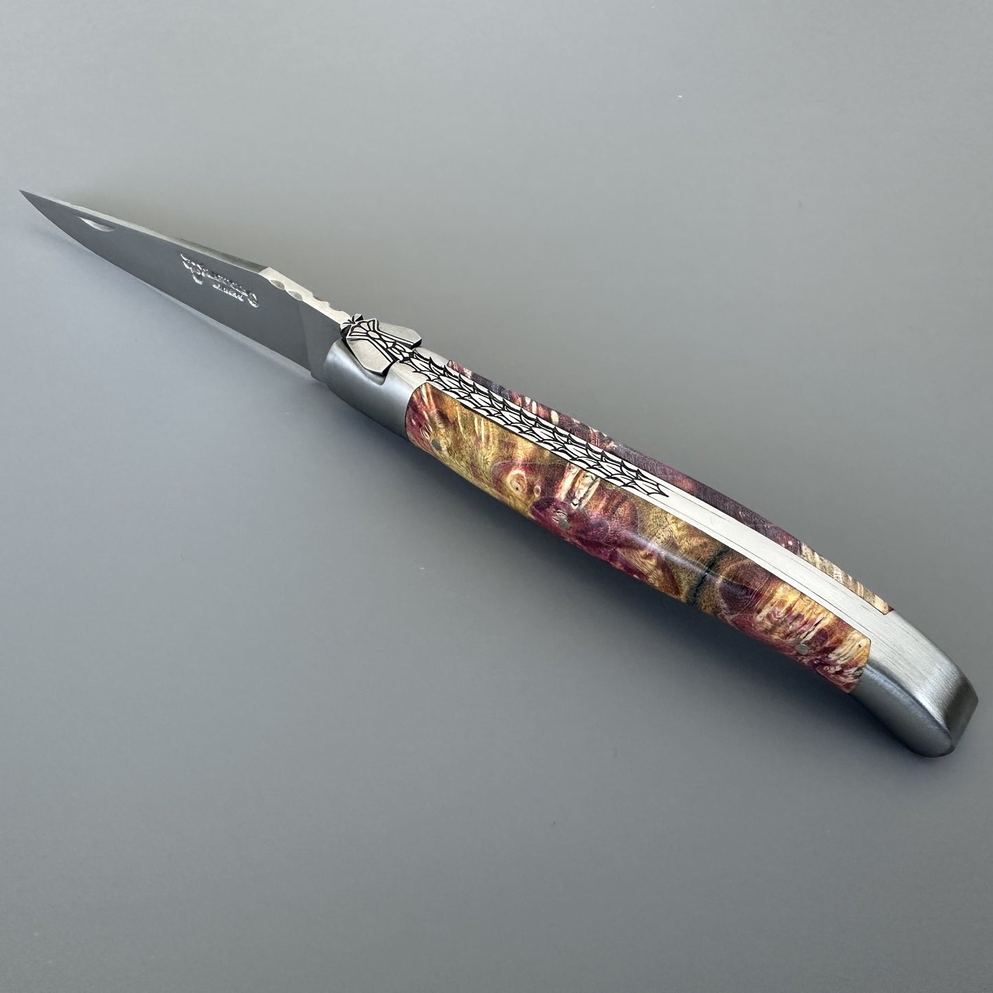 Open Belle folding knife with etched blade and hand-carved special bee bolster, red-gold elder burl handle, shown blade-left