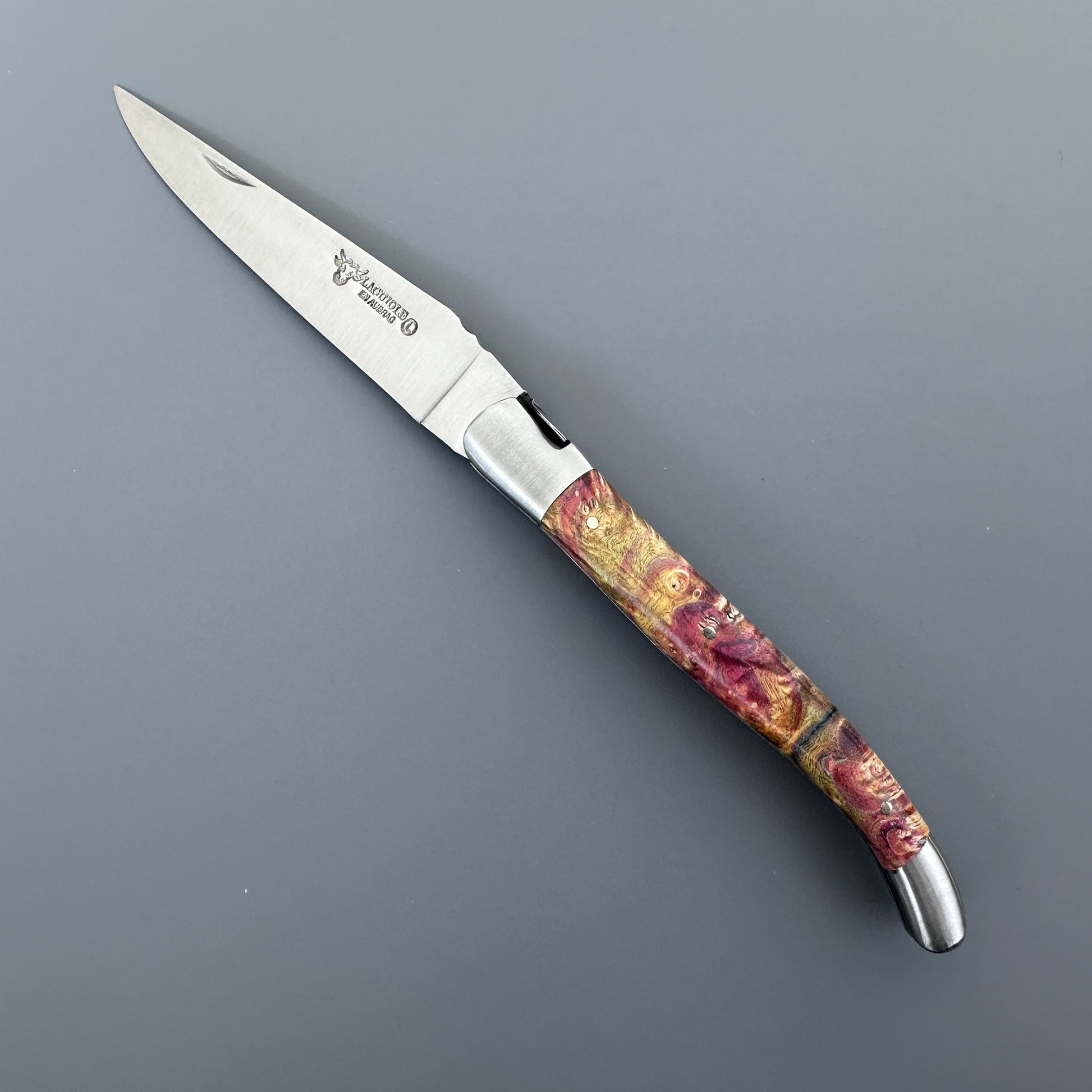Open Belle knife with etched blade and gold-burgundy elder burl handle, shown blade-right with maker's mark
