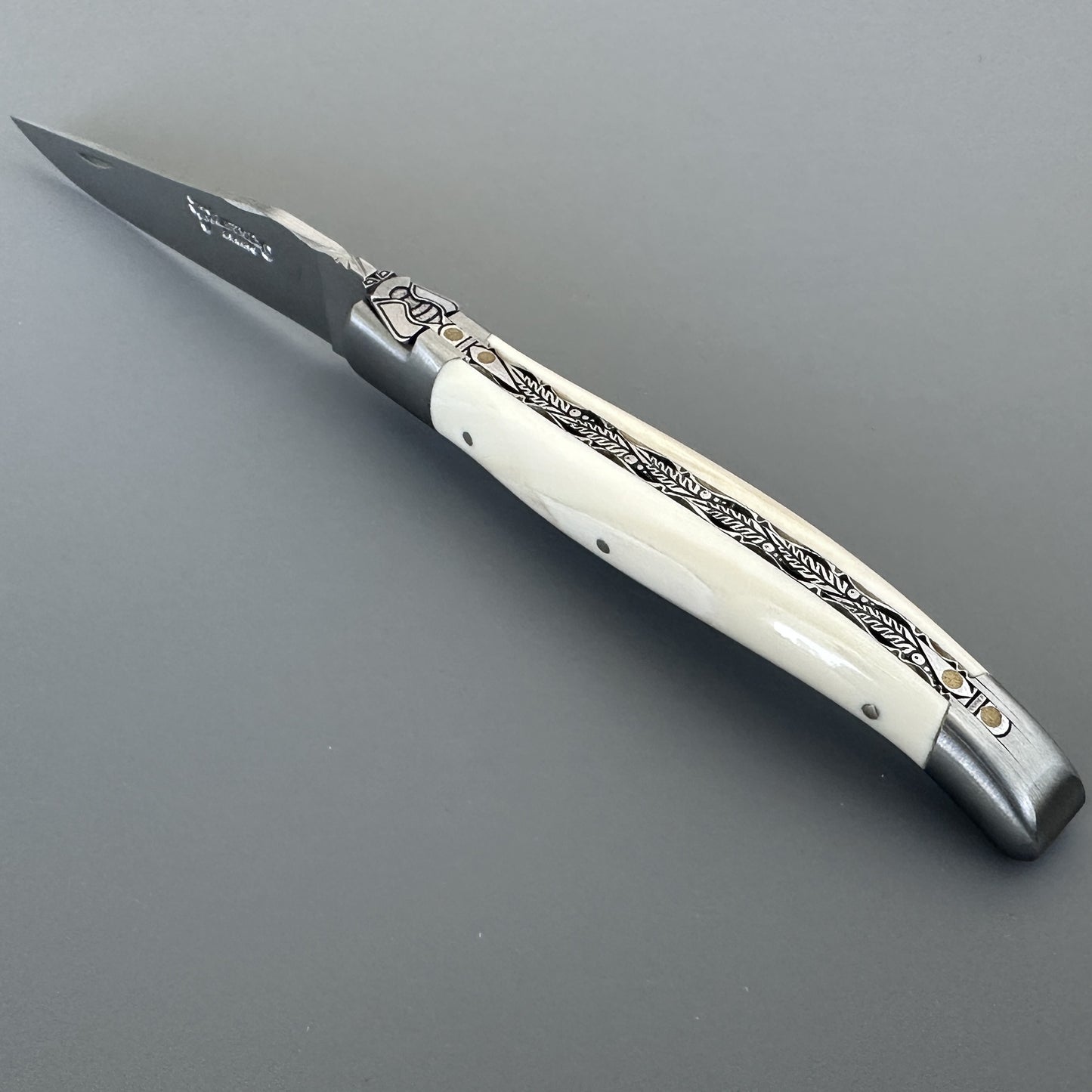 Angled view of the Belle knife's pointed blade and hand-carved bee emblem on the bolster