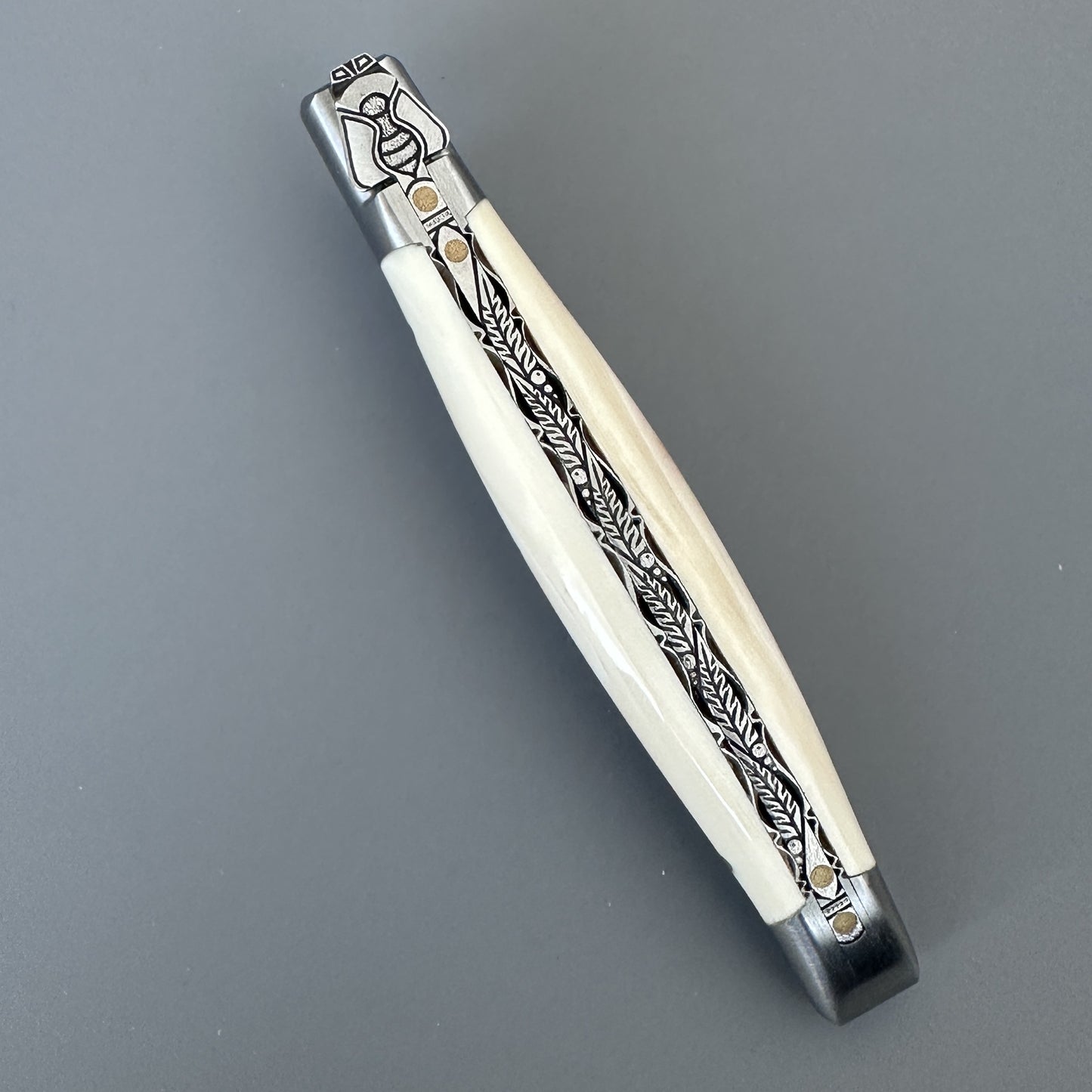 Closed Laguiole en Aubrac Belle folding knife with cream warthog bone handle and engraved bolster, full length