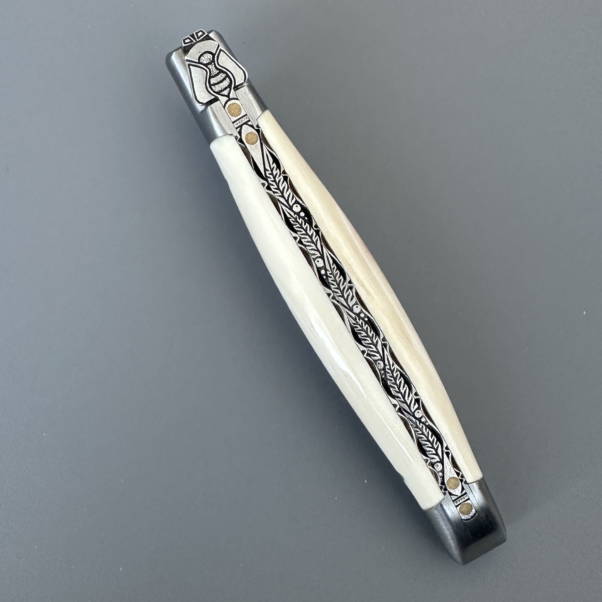 Closed Laguiole en Aubrac Belle folding knife with cream warthog bone handle and engraved bolster, full length