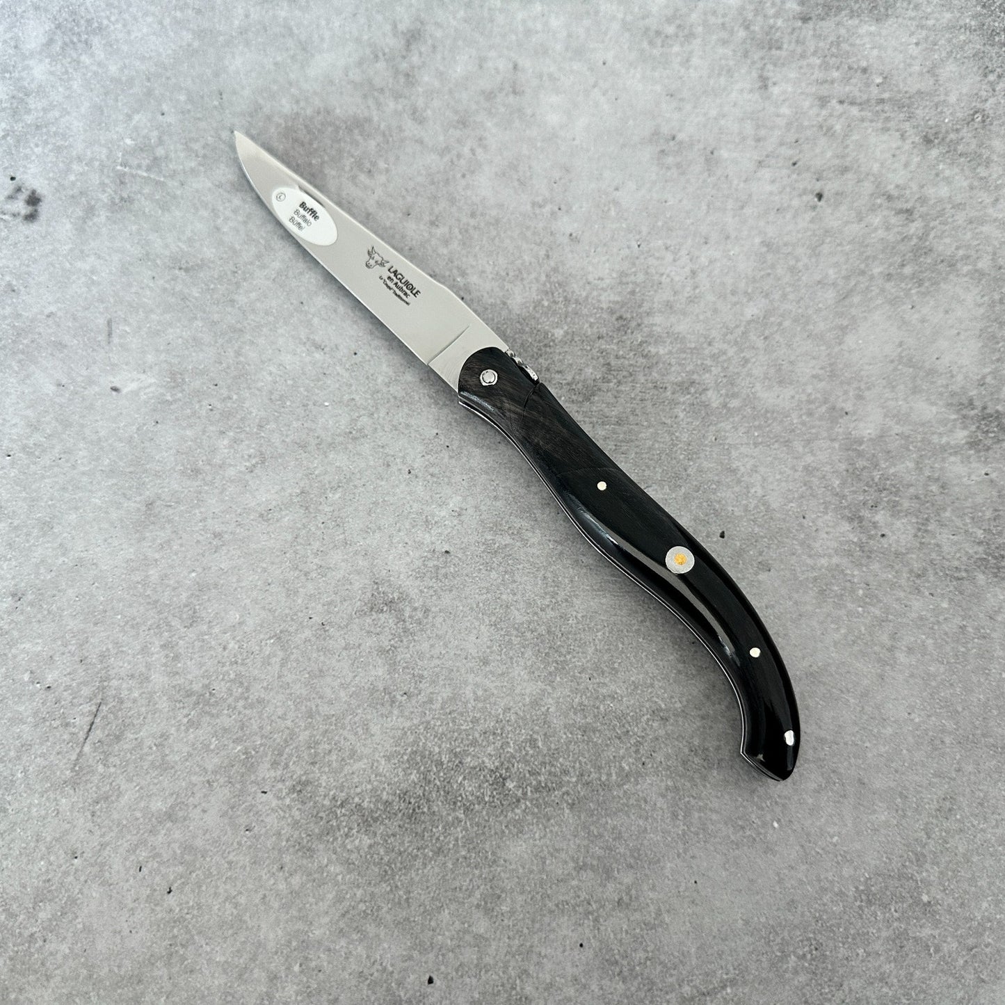 Laguiole en Aubrac folding knife with its black buffalo-horn handle and decorative emblem.