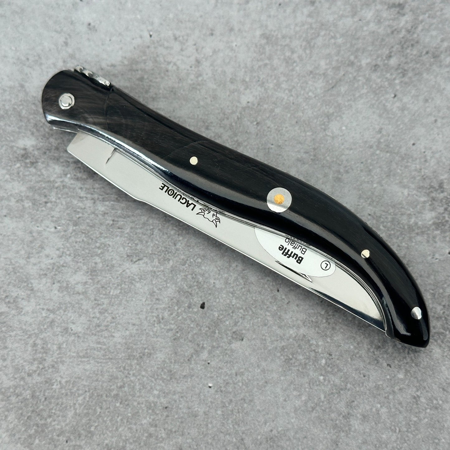 Closed Laguiole en Aubrac folding knife shown from an angled spine view with a polished buffalo-horn handle over concrete background