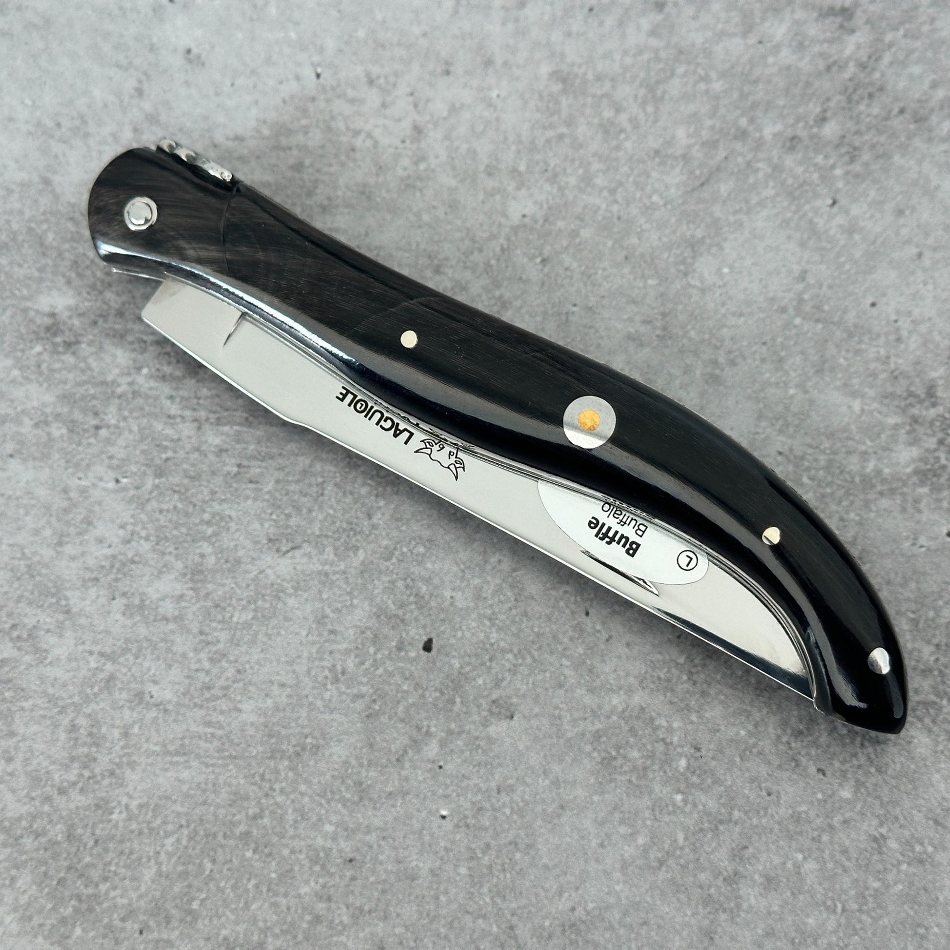 Closed Laguiole en Aubrac folding knife shown from an angled spine view with a polished buffalo-horn handle over concrete background