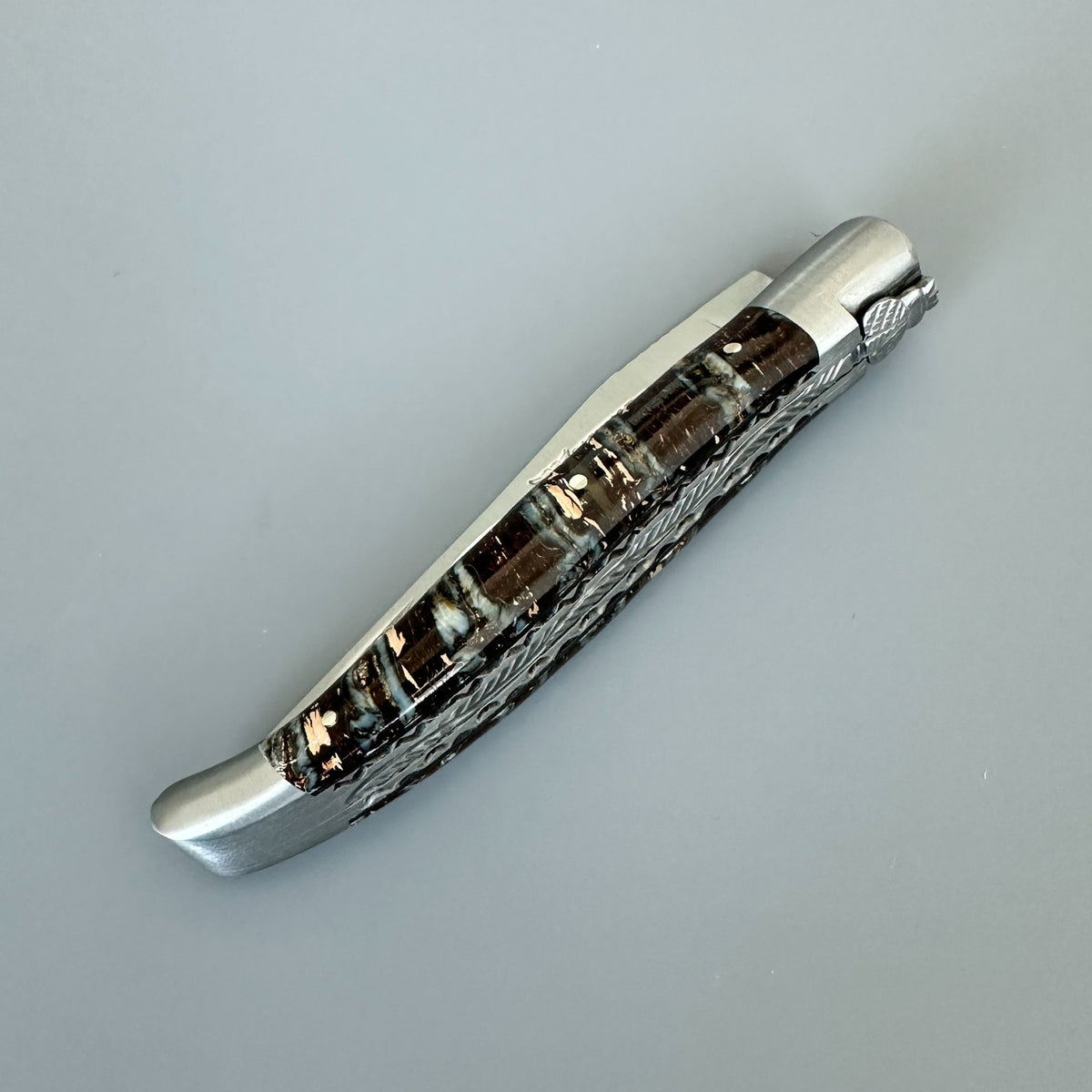 Closed Laguiole en Aubrac double-plated knife with brown mammoth molar handle and hand-decorated spine