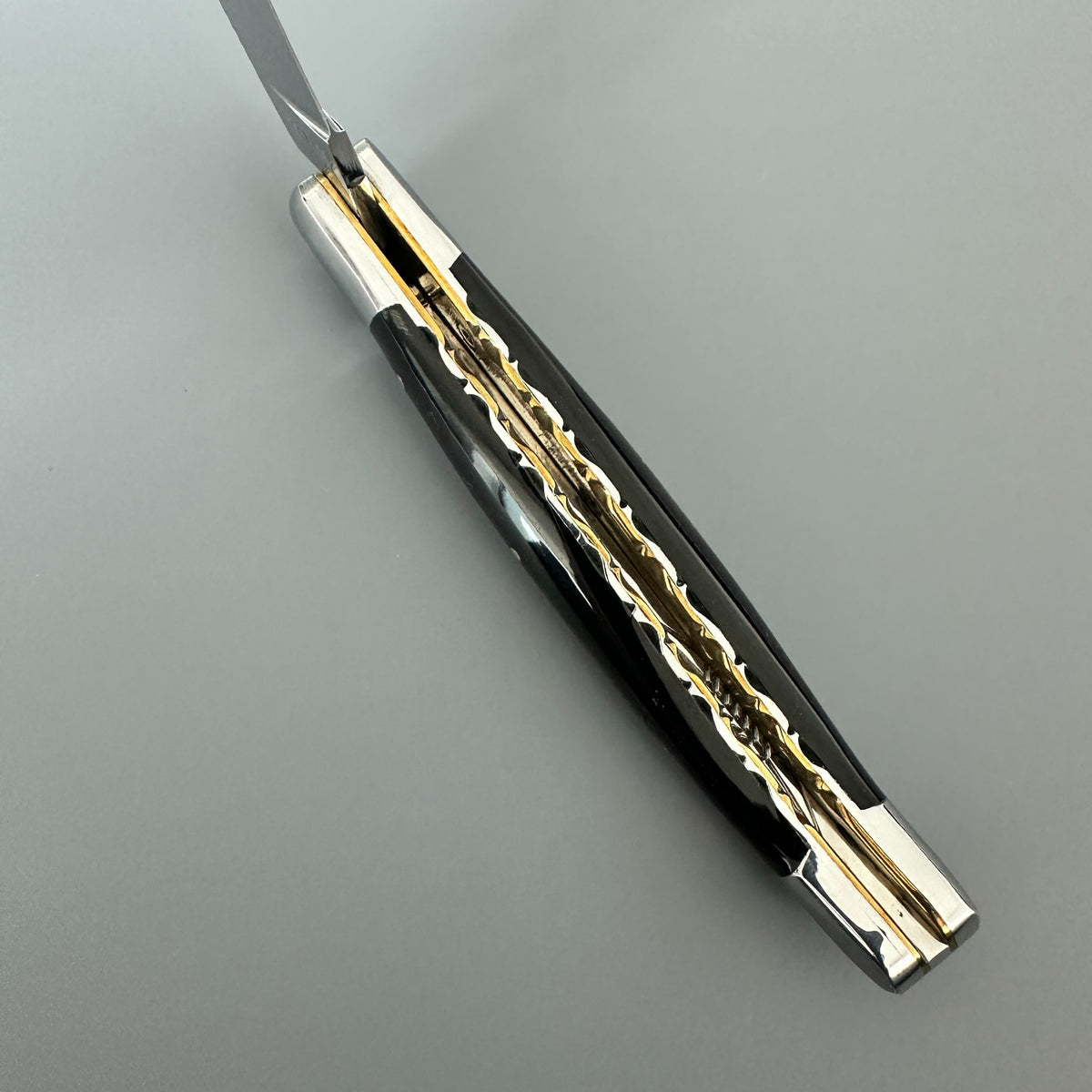 Laguiole en Aubrac double-plated pocket knife with a buffalo horn handle and polished silver-toned metal blades and brass inner spine, shown open on a neutral gray background.