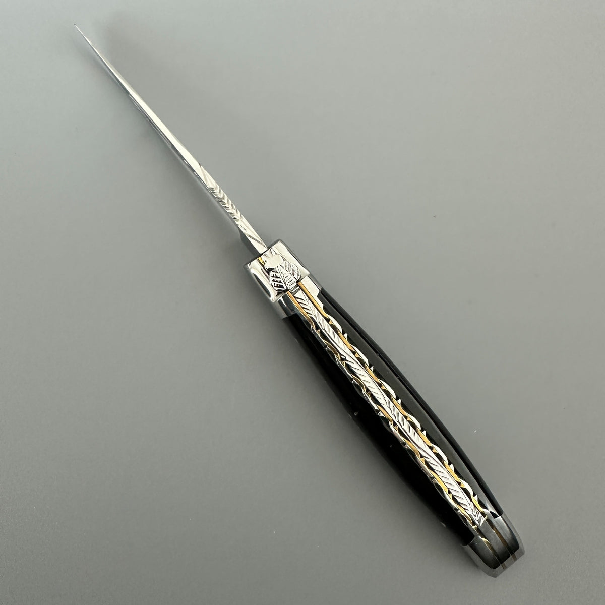 Laguiole en Aubrac double-plated pocket knife with a buffalo horn handle, featuring intricate gold-toned floral engravings on the metal collar and handle.