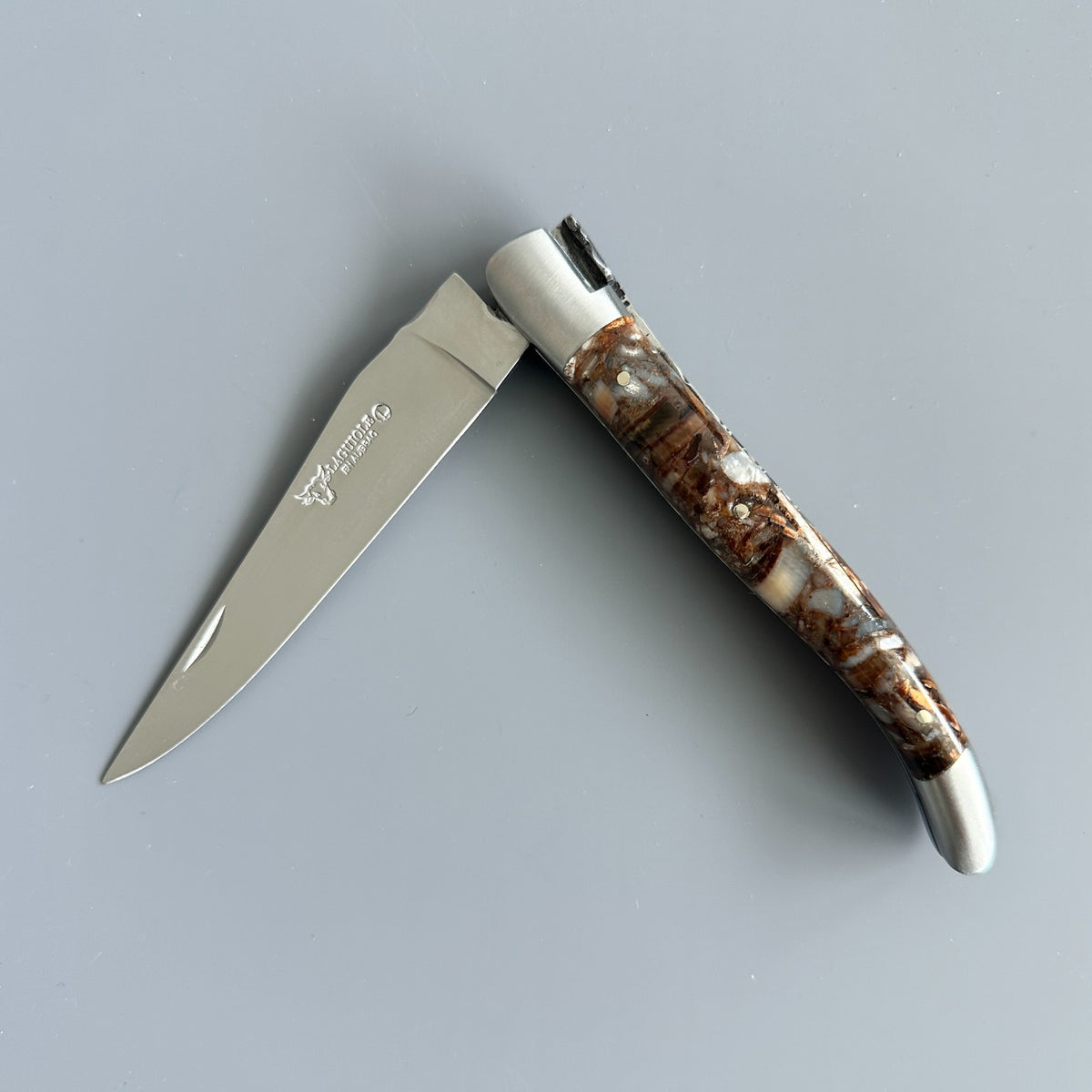 Laguiole en Aubrac Folding Knife with Brown Fusion handle partially opened over gray background