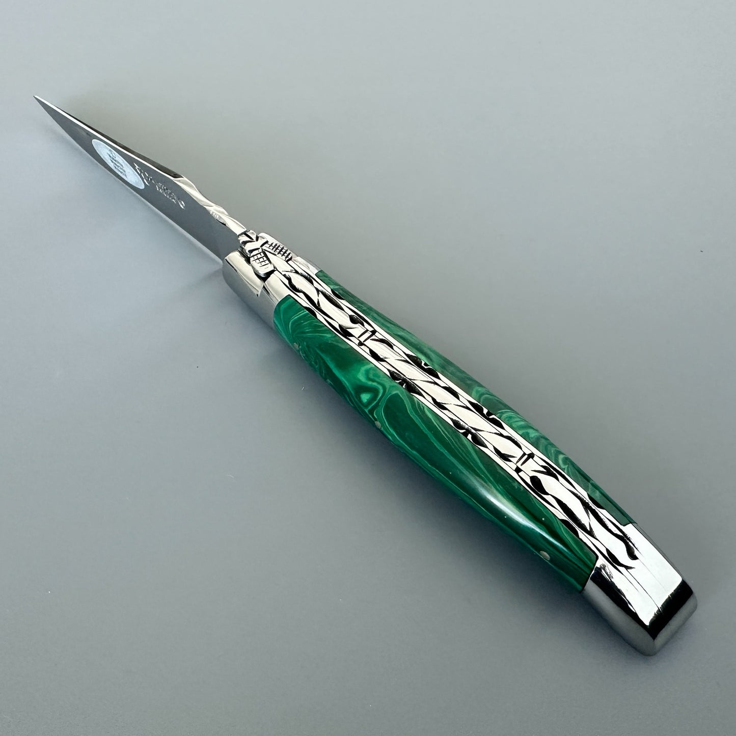 Angled spine view of a Laguiole en Aubrac double-plated knife with green malachite handle and file work