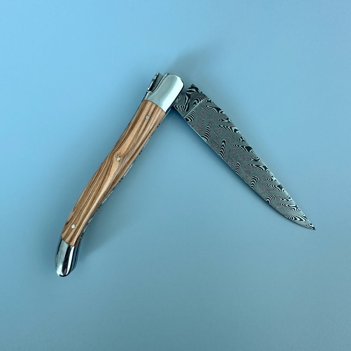 A folding pocket knife with a Damascus steel blade and a striped wood handle, shown open against a solid light blue background.