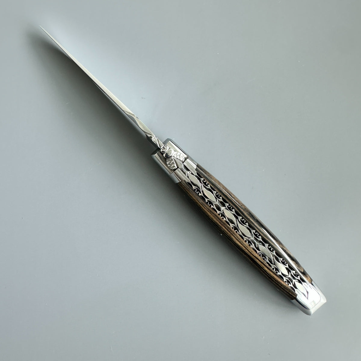 Laguiole en Aubrac pocket knife with  Royal Ebony handle featuring silver floral engravings, shown on a neutral gray background.