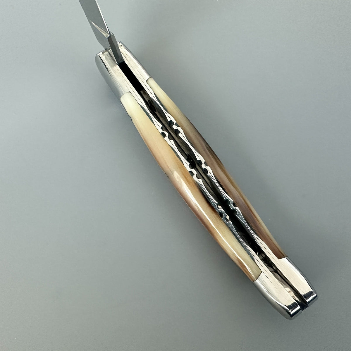 Inner side of Laguiole en Aubrac double plated pocket knife with solid horn flame handle ove a gray background