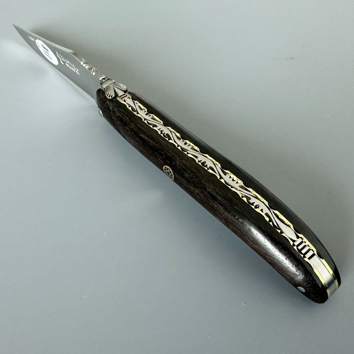 Laguiole en Aubrac folding knife with Ebony handle and brass mosaic pin over a dray background