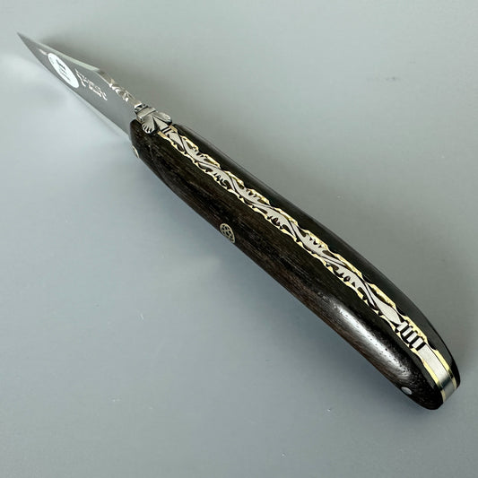 Laguiole en Aubrac folding knife with Ebony handle and brass mosaic pin over a dray background