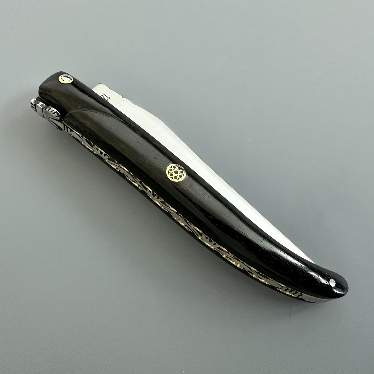 A Laguiole en Aubrac folding pocket knife with a Ebony handle handle, and gold-tone brass spine and a centered mosaic pin.