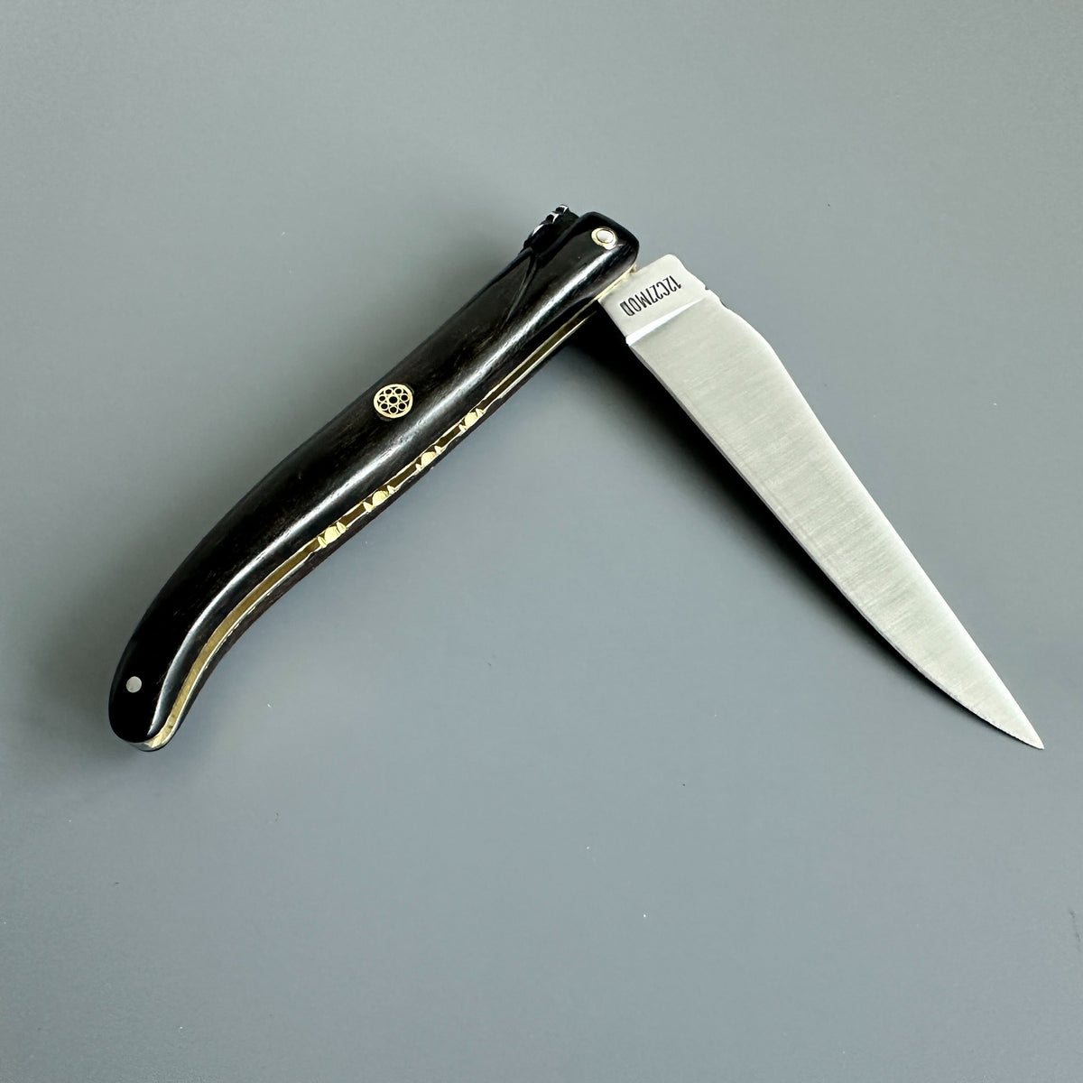 Laguiole en Aubrac folding knife with Ebony handle and brass mosaic pin partially opened.
