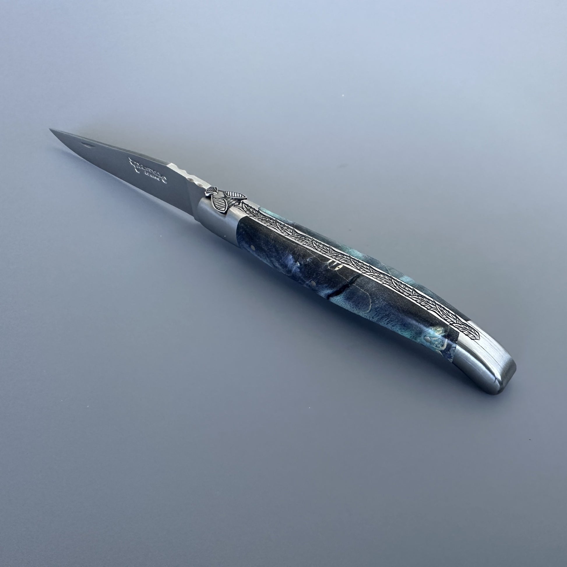 Open Laguiole en Aubrac pocket knife with elder burl handle and etched steel blade, shown blade-right with visible maker's mark
